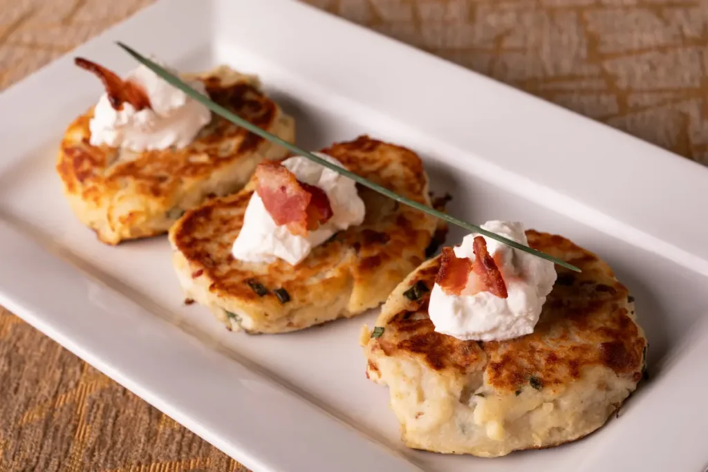 Three potato pancakes on a white platter, each topped with a dollop of sour cream and a piece of bacon.