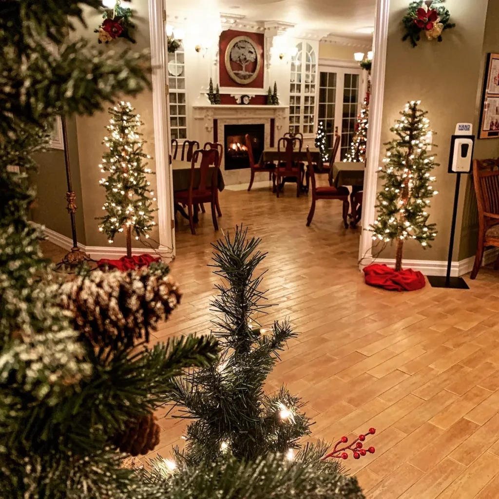 Festively decorated room with small lit Christmas trees and a fireplace in the background.