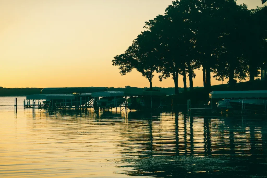 A sunset over a calm lake with silhouetted trees and boat docks reflected in the water.