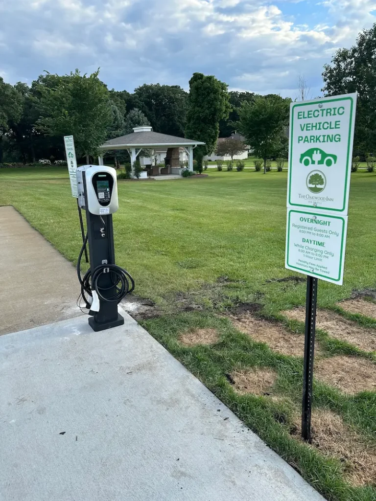 An EV charging station stands in a grassy park, next to an "Electric Vehicle Parking" sign.